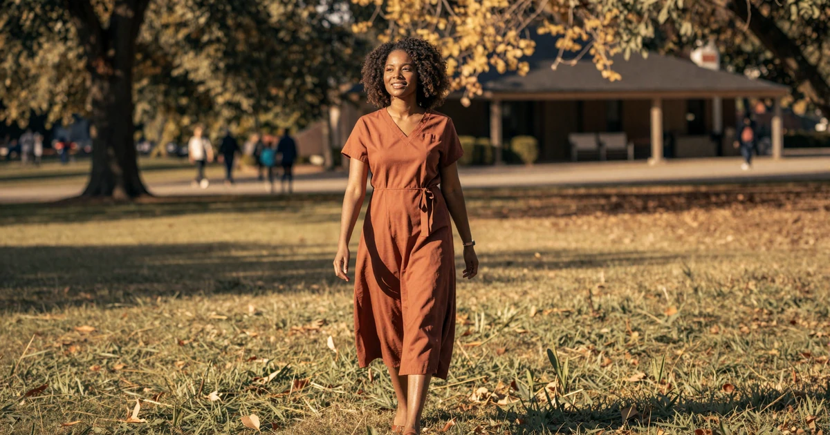 Confident female nurse midwife in a flowing dress walking in a sunlit park at golden hour